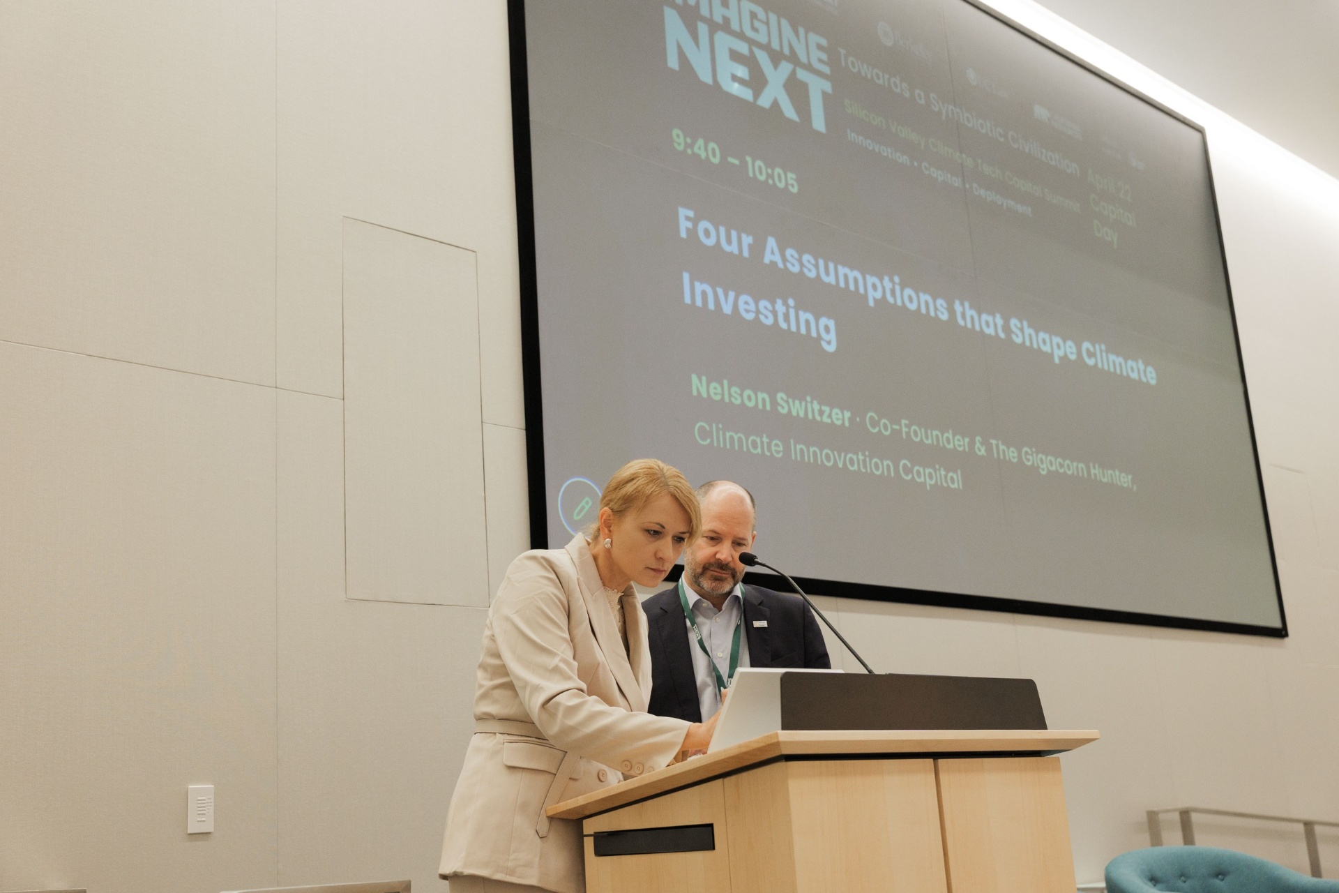 Speaker and host preparing at the podium beside the Capital Day keynote slide