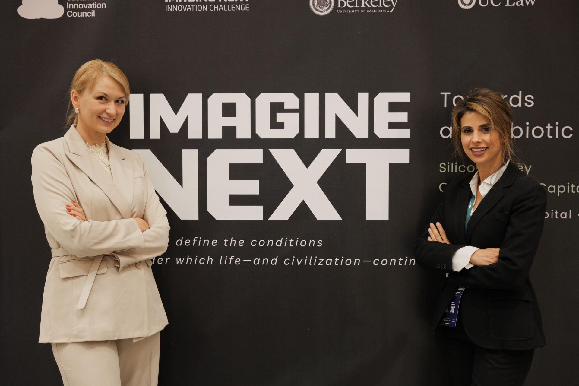 Julia Daviy and Mariam Amin JantzSell in front of the Imagine Next 'Towards a Symbiotic Civilization' backdrop at Capital Day, UC Law SF