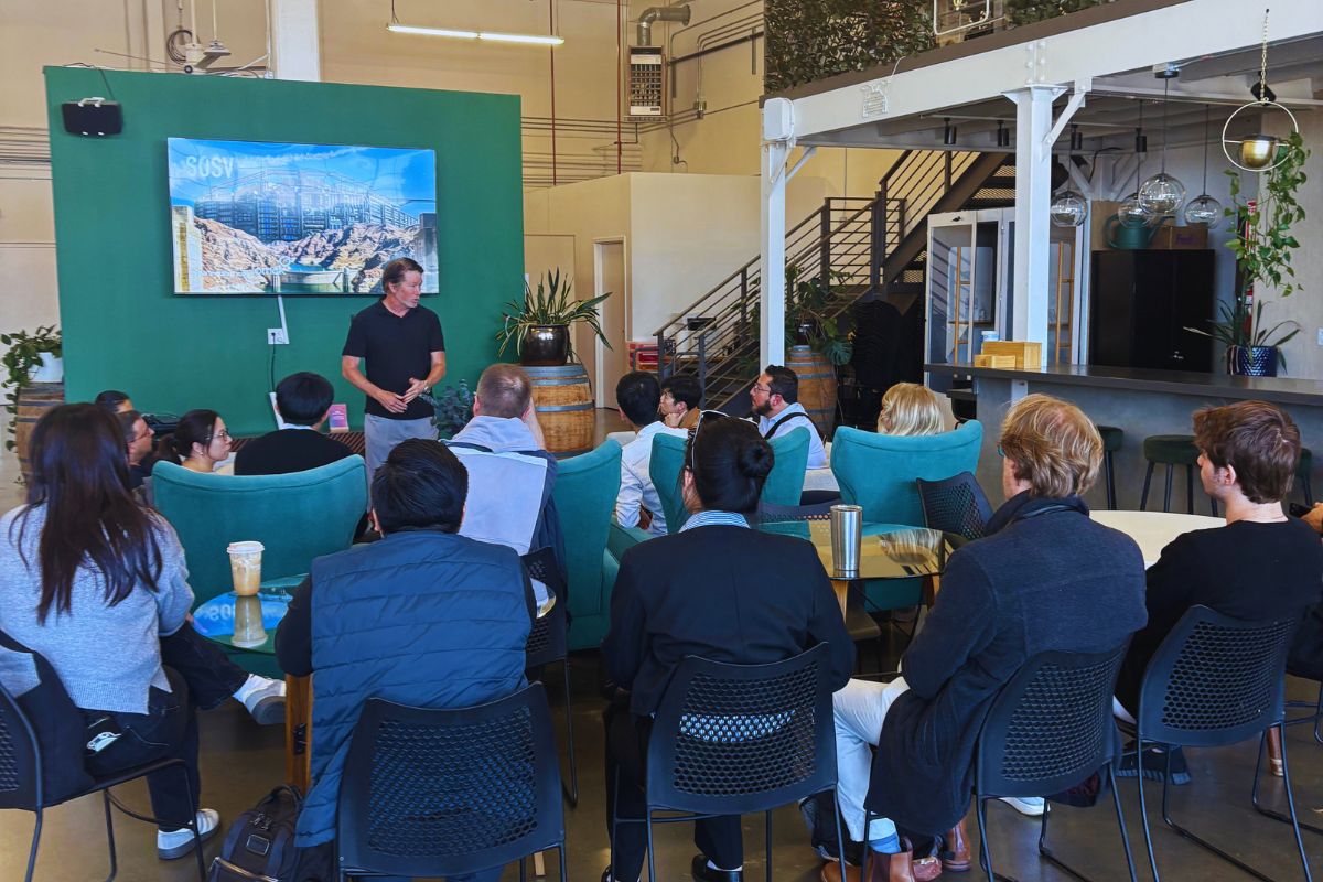 Frontiers Day at SOSV San Francisco — host addressing founders and investors in front of the green SOSV backdrop and Hoover Dam screen