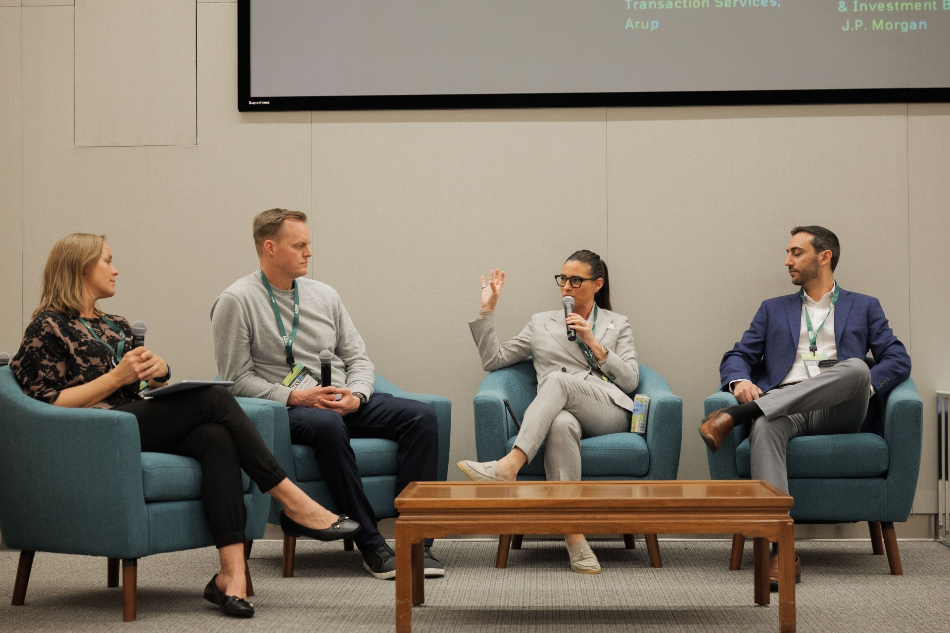 Capital Day built-environment finance panel at UC Law SF — moderator, Pete Gilchrist, Dr. Tobi Ann Petrocelli of Arup speaking, and Hatef Baradi of J.P. Morgan seated on stage beneath the speaker line-up slide