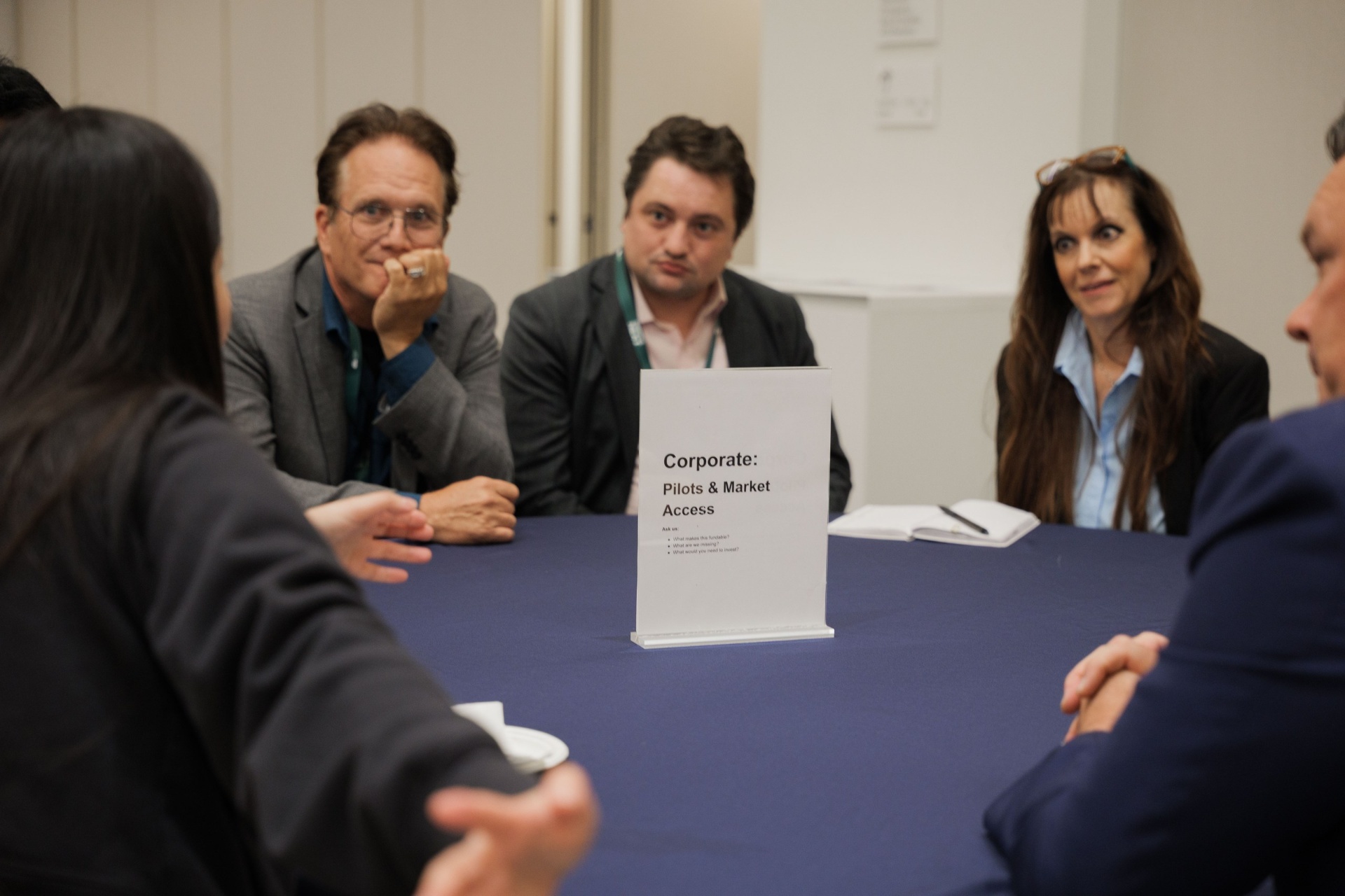 Capital Day Curated Capital Matchmaking Session — three delegates listening attentively at the 'Corporate: Pilots & Market Access' table at UC Law SF