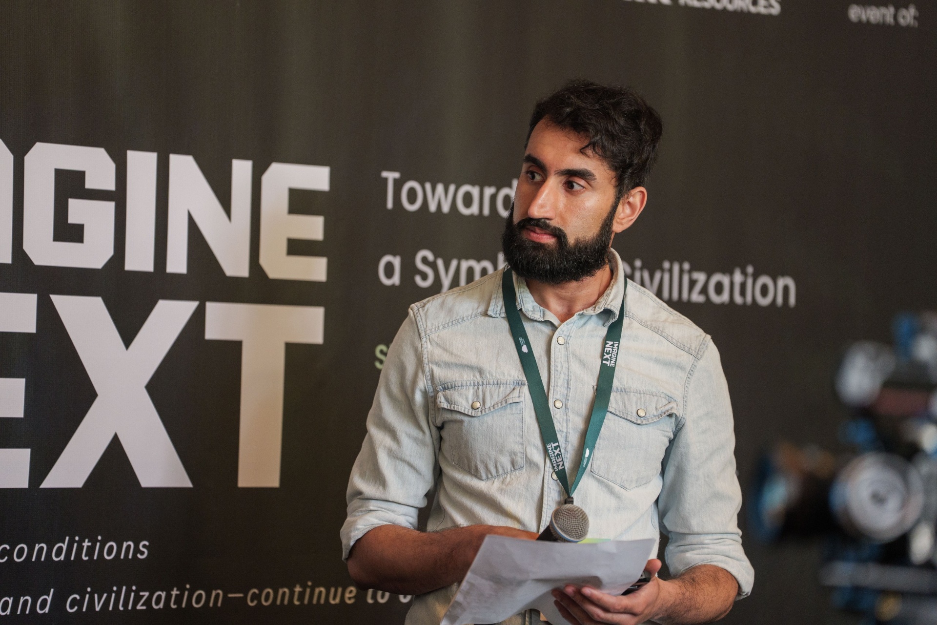 Founder in denim shirt addressing the audience by the Imagine Next banner